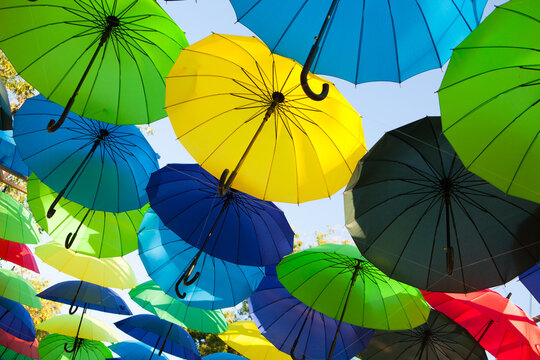 Bright umbrellas in green, yellow, blue, and red form an outdoor decorative display, festive creative background.