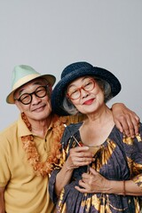 Fototapeta premium Happy senior couple embracing in sun hats and leis holding tropical cocktails for summer holiday portrait and lifestyle banner design