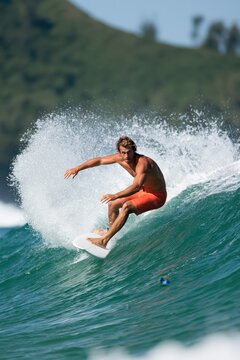 Male surfer carving a green wave with dramatic spray and motion for surfing action wallpaper and sports banner design