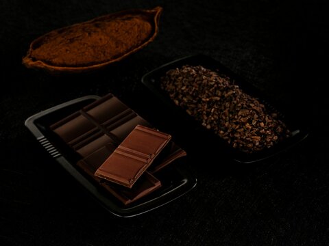 Elegant chocolate bars sit beside a bowl of rich cocoa nibs and powder, highlighting the essence of quality ingredients