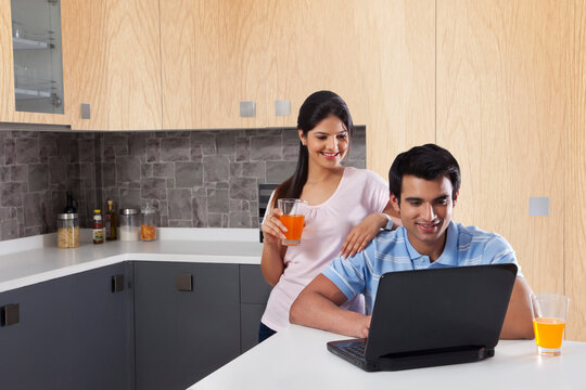 Couple using laptop while having juices in kitchen