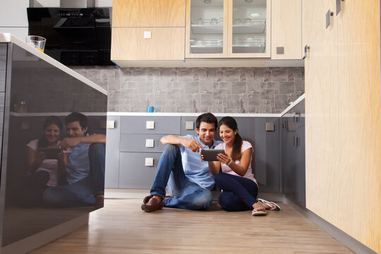 Full length of Indian couple using digital tablet in kitchen