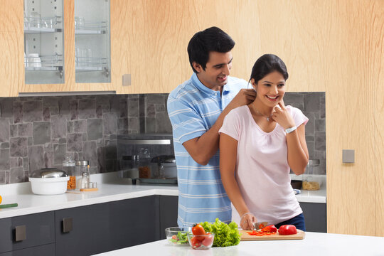 Young man fastening woman's necklace in kitchen