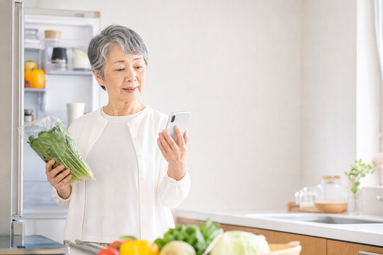 スマートフォンを見ながら冷蔵庫の食材を確認する日本人シニア女性