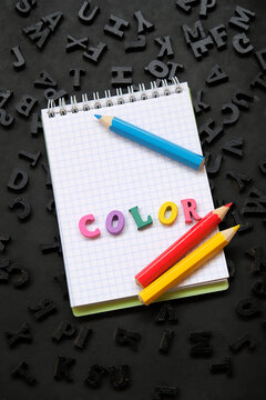 notepad, colored pencils, text "color" made of colorful letters and many black alphabet letters on abstract black background close up. element for creative project and modern design. minimal style