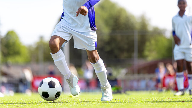 Low Angle View of Junior Soccer Player Dribbling Ball on Pitch - Close-Up Action of Footwork and Cleats During Youth Football Match