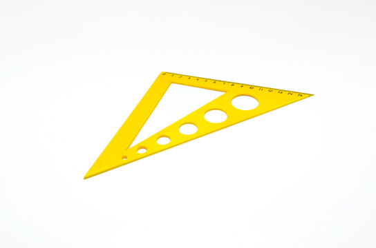 Yellow plastic set square with measurement scale and circular holes on white background. Isolated geometry tool for mathematics education, technical drawing and school supplies.