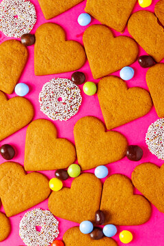 Top view of candies and heart shaped cookies on a vibrant pink background. Dessert photography, sweet treats.