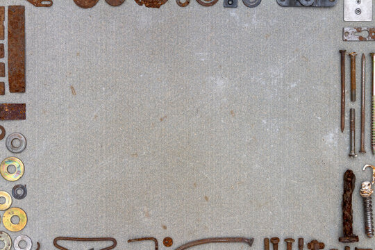 A frame of various old rusty bits and pieces arranged on a concrete surface. Old rusty nuts, bolts, nails and other parts flay lay on gray background.