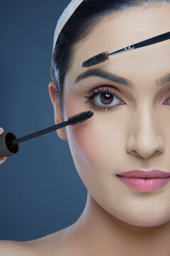 Cropped image of an attractive young woman with mascara and eyebrow tinting applicator over colored background 