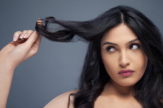 Attractive young woman twisting hair around her finger over colored background 