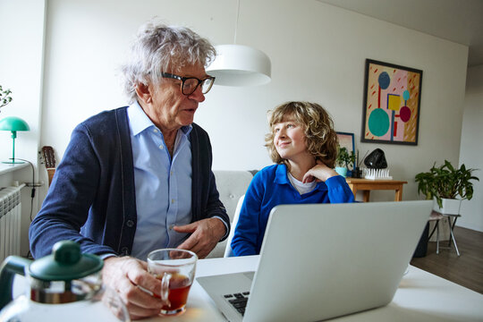 Senior man and teenage boy talking together while spending time together at home