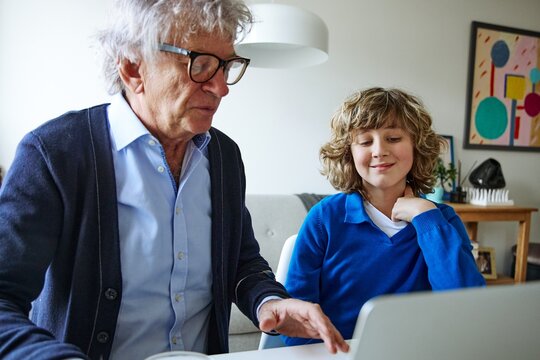Senior man and teenage boy using laptop during an everyday family activity at home