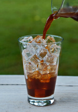 Close-up of iced Americano coffee being poured into a clear glass filled with ice cubes