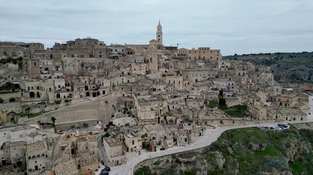 Aerial view of the historic Sassi di Matera with ancient stone dwellings, winding narrow streets, and a prominent church tower overlooking the ravine in Matera, Basilicata, Italy.