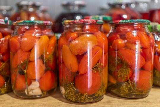 Row of glass jars with homemade preserved red tomatoes close up