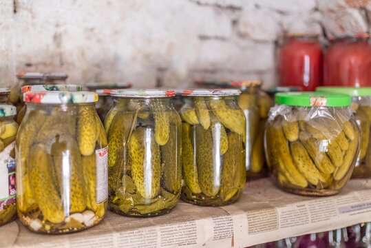 Glass jars filled with pickled cucumbers on pantry shelf close up