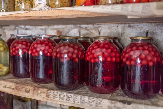 Large glass jars with homemade sweet cherry compote on pantry shelf