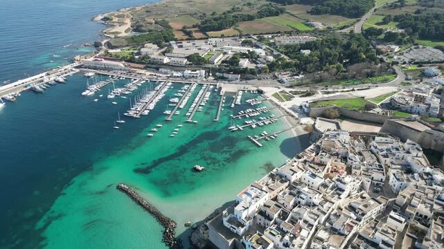 Aerial view of the historic harbor and old town of Otranto with turquoise waters, docked boats, and stone fortifications in Otranto, Apulia, Italy.