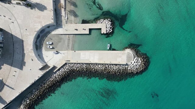 Aerial view of the stone pier and small boats in the turquoise waters of the harbor in Otranto, Apulia, Italy.