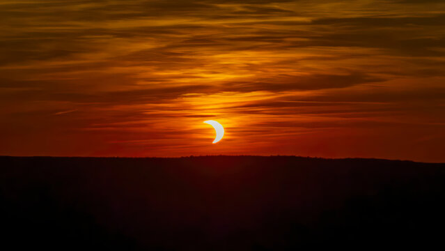 artial solar eclipse during sunset, rare sunset with orange dramatic sky.