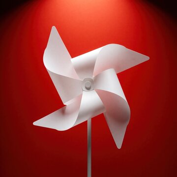 White paper pinwheel stands on red background. Minimalist toy windmill with four blades creates simple geometric shape. Playful summer object for kids decoration. Bright studio shot with clean pop
