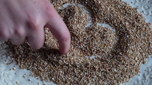 Person's finger tracing a heart symbol in a pile of dry buckwheat groats on a decorative plate