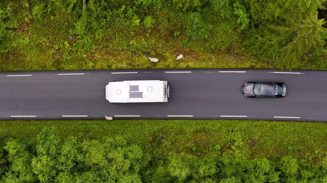 Aerial view of a white camper van and other cars driving on a road through a lush green forest with sheep grazing nearby in Valldal, More og Romsdal, Norway.