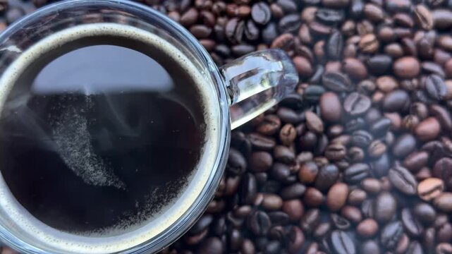 Glass cup of black coffee surrounded by roasted coffee beans, hot morning drink, cozy atmosphere.