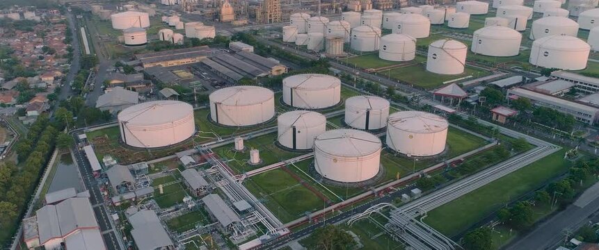 Aerial view of large white oil storage tanks at a refinery facility with industrial piping and paved roads in Cilacap Regency, Central Java, Indonesia.