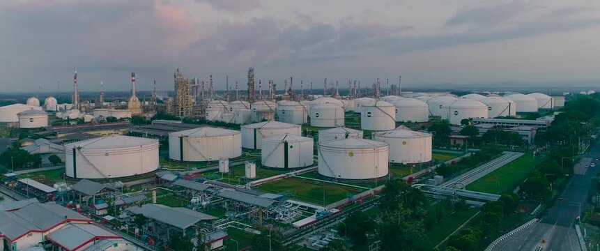 Aerial view of industrial oil refinery with large white storage tanks and processing facilities at sunset in Cilacap Regency, Central Java, Indonesia.