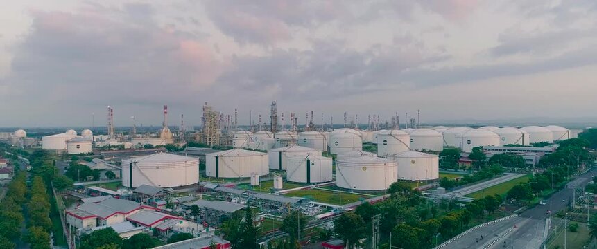 Aerial view of large industrial oil refinery with numerous white storage tanks and processing infrastructure surrounded by lush greenery in Cilacap Regency, Central Java, Indonesia.