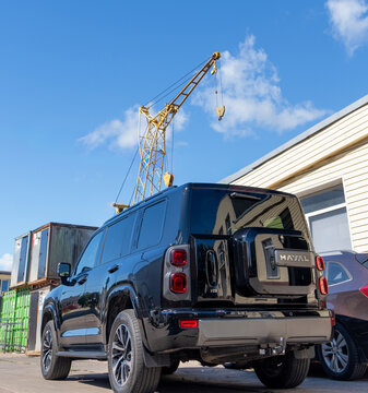 Black modern Haval H9 SUV car parked on an urban street near warehouse building and cargo crane against blue sky, exterior rear view of chinese off-road vehicle, contemporary lifestyle transport. SUV.