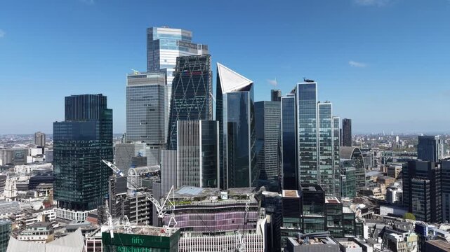 Aerial view of the modern City of London skyline featuring glass skyscrapers and construction cranes under a clear blue sky in London, England, United Kingdom.