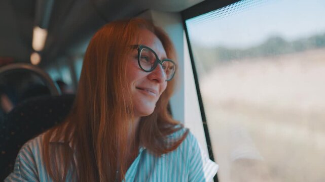 Woman smiles while looking out the window on a train ride in a rural area during daytime