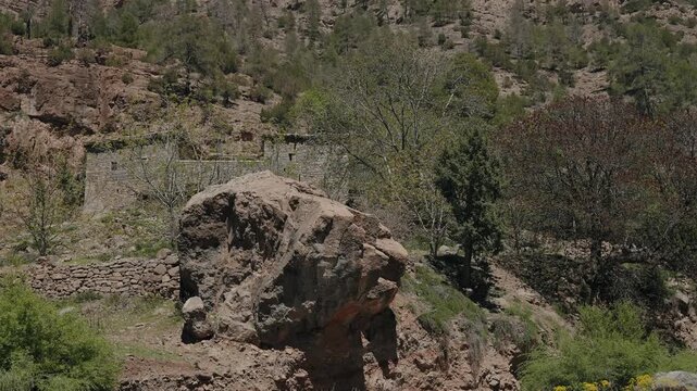 Large boulder on a terraced mountain slope below stone houses and juniper trees