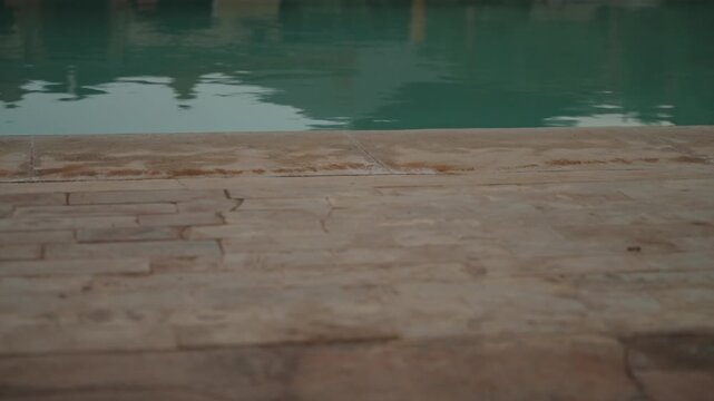 Weathered stone paving at the edge of a pool with still green water and reflections