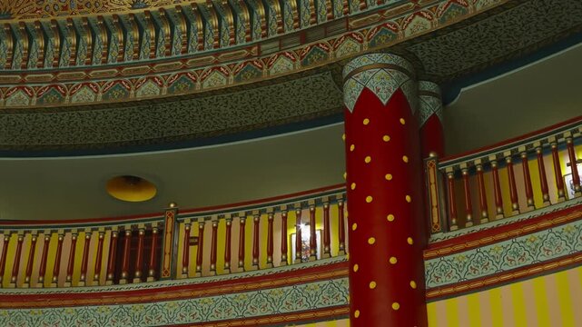 Red column with gold dots beside a curved balustrade under a painted carved ceiling