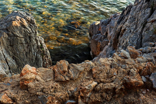 Coastal rocks shaping a rugged shoreline and forming a narrow channel over clear ocean water with visible underwater textures