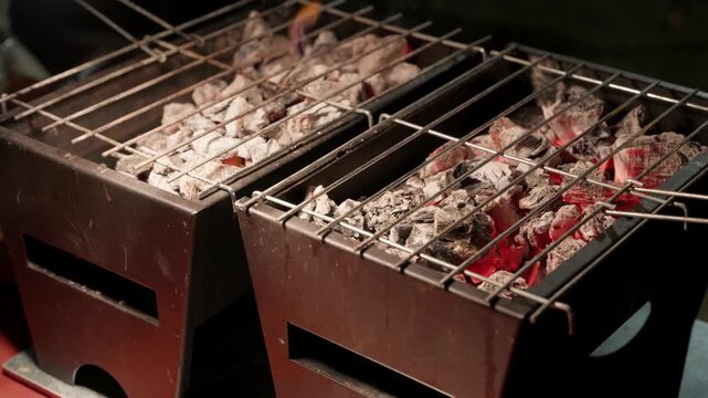 Grey ash covered charcoal glowing red under empty wire grates on a metal barbecue