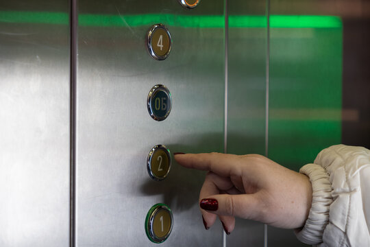 A person presses the elevator button for the second floor inside a modern building, illustrating daily urban commutes, vertical transport access, and simple routine travel navigation