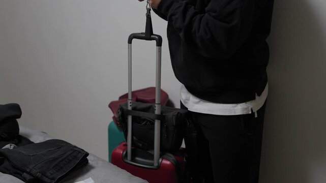 Person lifting a suitcase with a handheld luggage scale to check baggage weight indoors