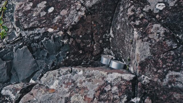 A static close up shot shows two small metal tea light candles nestled in the crevices of a dark, textured rock face.