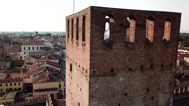 Close-up aerial view of a medieval brick tower in Montagnana, Veneto, with terracotta rooftops and open countryside behind it.