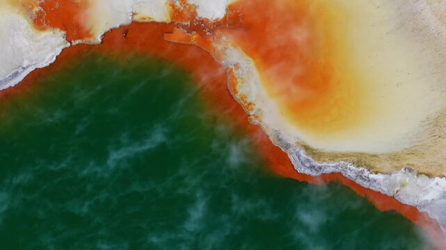 Top-down aerial view of a vibrant geothermal hot spring in Rotorua, Bay of Plenty, New Zealand, showcasing vivid mineral colors, steaming turquoise water, and striking volcanic formations.