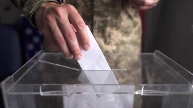 US soldier in camouflage moving and inserting ballot into box, American flag background