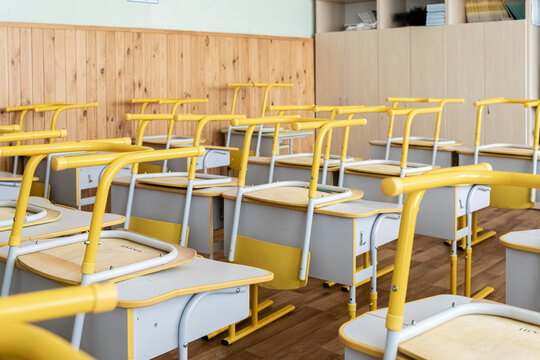 An empty primary school classroom features yellow desks stacked with chairs placed on top to reflect the quiet academic downtime during a long summer vacation break for students