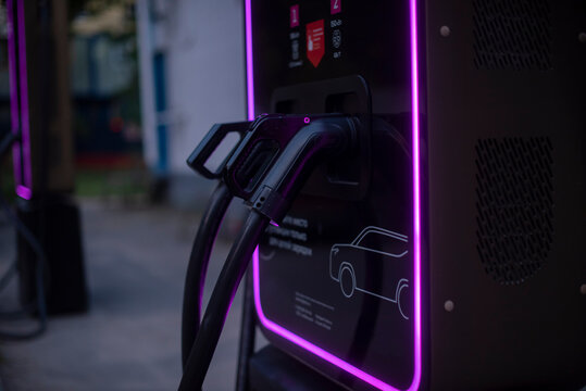 Electric car charging station with a charging cable connected. The station features modern design and illuminated edges, emphasizing sustainable energy use.