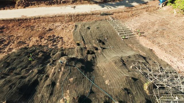 Workers strengthen the slope of the mountain with metal mesh preventing rockfall and landslide on the road, above view. workers constructing anti-landslide concrete wall prevent protect against rock