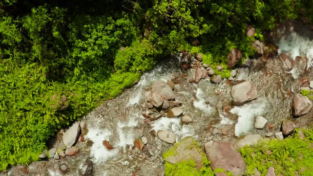 Mountain river with large stones in the rainforest, aerial view. River in the green forest. River flowing through boulders, Camiguin, Philippines.